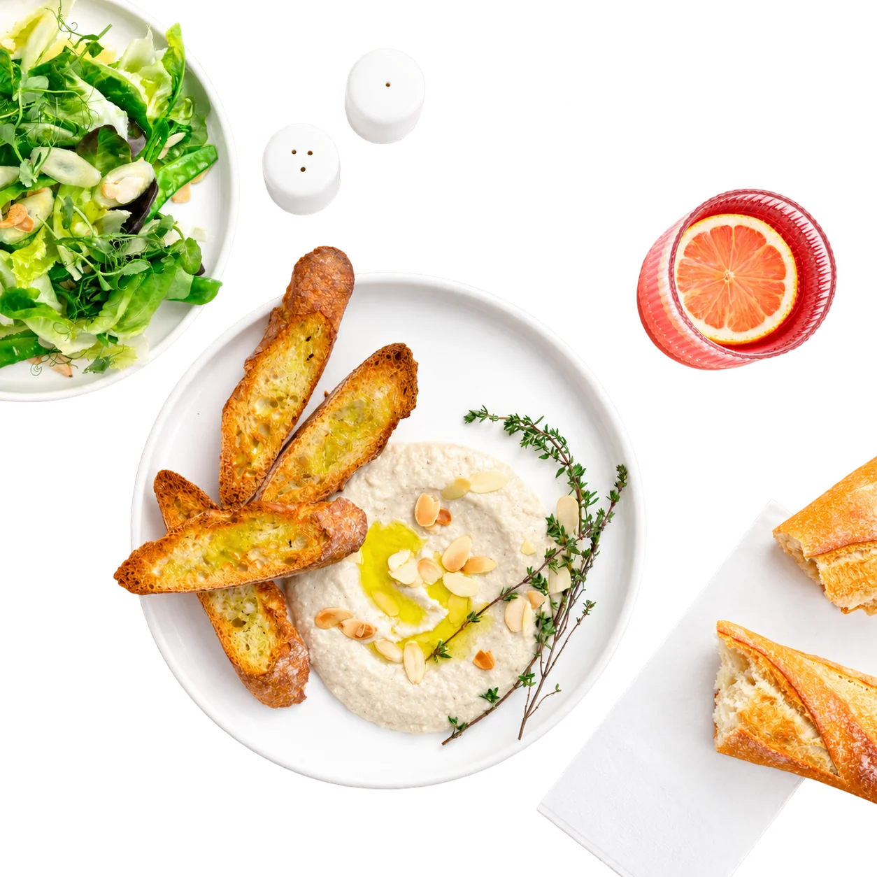 Vue de dessus d'une assiette blanche de crème onctueuse aux amandes effilées et thym, accompagnée de tartines grillées, d'une salade verte, d'un verre au pamplemousse et de pain.